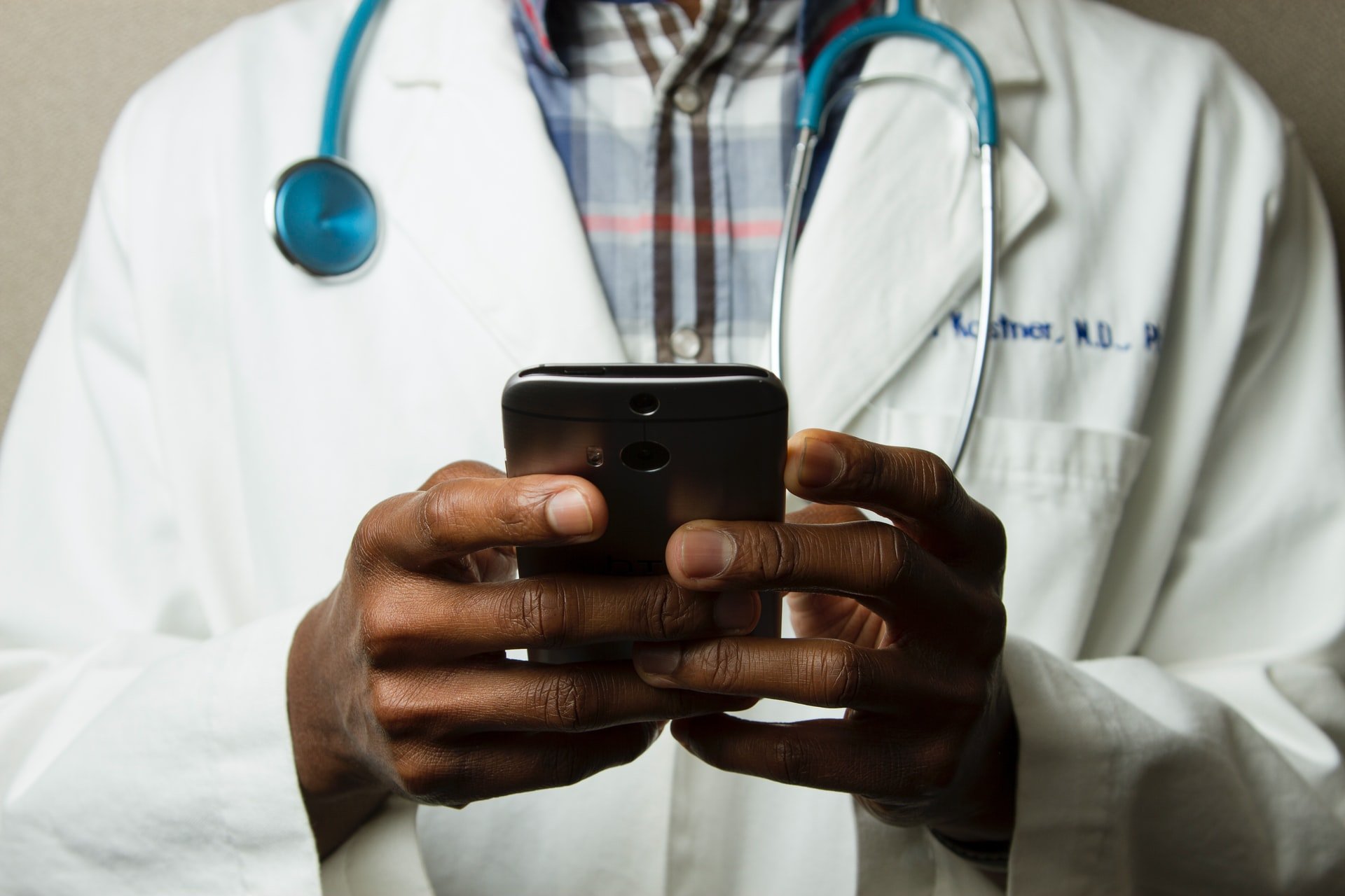 Doctor using phone with stethoscope around neck. Photo by National Cancer Institute on Unsplash